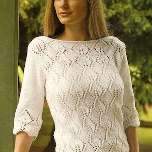 Può includere: Un maglione bianco a maniche a tre quarti con scollo a barchetta. La maglieria presenta un motivo traforato dettagliato a forma di diamante e disegni a forma di foglia. Le maniche e l'orlo hanno un bordo smerlato.