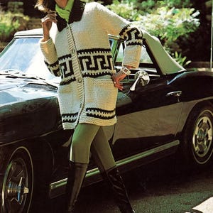 May include: A cream-coloured knitted cardigan with black geometric patterns, worn with olive green leggings and black knee-high boots. The outfit is completed with a green scarf and a silver watch. A vintage black convertible car is in the background. The cardigan's length is approximately 80 cm.