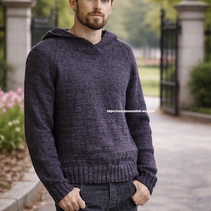 May include: A dark gray hooded sweater with long sleeves. The sweater has a ribbed hem and cuffs. The person in the image is wearing dark gray jeans. The background includes a gate and trees.