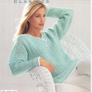 Könnte beinhalten: Ein helltürkisfarbener Häkelpullover mit langen Ärmeln und weißem Besatz. Der Pullover hat einen Rundhalsausschnitt mit weißer Krawatte. Das Bild stammt aus einem Vintage-Musterbuch. Der Text "Patons Classics" steht oben.