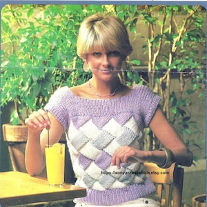 May include: A knitted top with a geometric diamond pattern in shades of lavender, white, and gray. The top has a boat neck and short sleeves. The image also shows a glass of orange juice with a lemon slice and a website address.