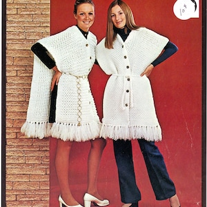 May include: Two women wearing white crochet capes with button closures and fringe trim. One cape has a long, flowing design, while the other is a shorter, belted style. The women are standing in front of a red background.