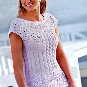 May include: A light purple knitted top with a round neckline and short sleeves. The top features a detailed cable knit design down the front and a decorative openwork pattern at the neckline and hem. The top is made of a soft, lightweight material.