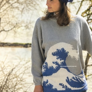Könnte beinhalten: Ein grauer, langärmeliger Strickpullover mit einer großen blau-weißen Grafik einer brechenden Welle auf der Vorderseite. Der Pullover hat einen Rundhalsausschnitt und gerippte Bündchen. Der Text https://sonyacrossstitch.etsy.com ist auf der Welle abgebildet.