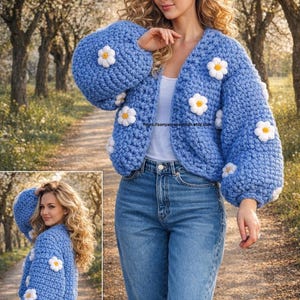 May include: A sky blue, chunky knit cardigan decorated with white and yellow daisy appliqués. The open-front sweater has long, puffed sleeves. The image also shows a woman wearing blue jeans. The Etsy shop URL is visible.