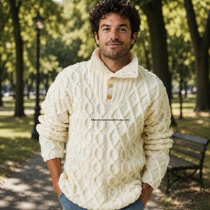 Peut inclure: Un pull en tricot torsadé blanc cassé doté d'un col montant avec deux boutons à l'encolure. Le vêtement présente un motif texturé en losanges et en cordes sur tout le corps et les manches, associé à un jean bleu.