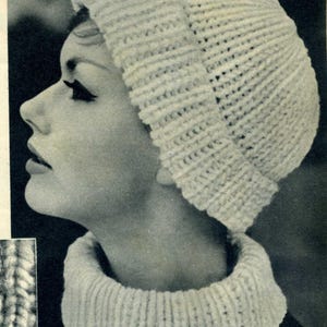 May include: A knitted white hat and cowl set. The hat is a close-fitting beanie style, and the cowl is a wide, ribbed neck warmer. The set is made of a textured, possibly wool, yarn. The image is in black and white.