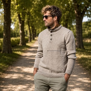 May include: A beige long-sleeve knit sweater featuring a mock neck collar with three buttons, paired with light olive green trousers. The sweater has ribbed cuffs and a ribbed hem, and the text https://sonyacrossstitch.etsy.com is visible.