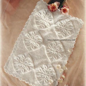 Può includere: Una coperta quadrata bianca all'uncinetto con un motivo floreale. La coperta presenta disegni floreali tridimensionali in rilievo e un bordo smerlato. L'URL del negozio Etsy è visibile nell'immagine.