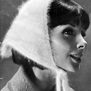 以下が含まれることがあります： 白くふわふわしたニットのヘッドカバーを身につけた女性の白黒ポートレート。ヘッドカバーは頭にかけられ、あごの下で結ばれています。女性は微笑んでおり、質感のあるコートを着ています。