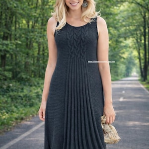 Könnte beinhalten: Dunkelgraues Strickkleid mit Zopfmuster-Oberteil und Faltenrock. Das ärmellose Kleid ist knielang und wird mit einem weißen Hut mit schwarzem Band getragen. Die Frau hält eine kleine Tasche.