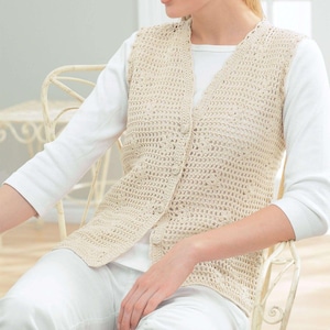 May include: A cream-coloured, open-weave crochet vest with a V-neck and button closure. The vest is worn over a white long-sleeved shirt. The crochet pattern creates a textured, airy design. The vest is a neutral colour, suitable for layering.