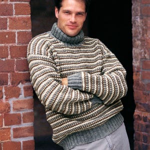 May include: A gray, brown, and white striped turtleneck sweater. The sweater has a ribbed texture and a thick, folded collar. The sleeves and bottom hem are solid gray. The person is leaning against a red brick wall.