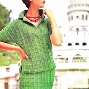 May include: A vintage green knitted two-piece outfit. The top has a collared neckline and short sleeves. The skirt is a pencil skirt style. The outfit is a solid green colour with a textured, grid-like pattern. A red beaded necklace is worn.