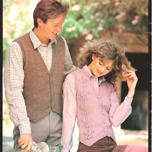 May include: A couple is shown wearing knitted vests. The man's vest is brown, and the woman's is pink with a leaf design. Both vests are button-down and worn over collared shirts. The background is a blurred outdoor scene.