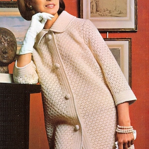 May include: A vintage cream-colored crochet coat with a button-up front and a collar. The coat is worn with white gloves and a pearl bracelet. The image has a retro aesthetic, with a woman posing in front of a red wall.