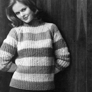 May include: A black and white photograph of a person wearing a striped knit sweater with a high neckline. The sweater features horizontal stripes in varying shades of gray and white. The person is leaning against a wooden wall.