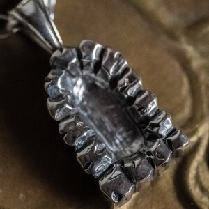 May include: Silver pendant necklace featuring a detailed, textured design of a religious figure. The pendant is shaped like a small shrine with a figure inside.