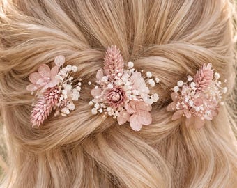 May include: Three hair pins featuring arrangements of dried flowers in shades of soft pink and white. Each pin contains a mix of small blossoms, delicate baby's breath, and textured grasses, secured into a half-up wavy blonde hairstyle.
