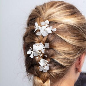May include: A blonde woman with a French braid in her hair. The braid is decorated with white flower hair clips.