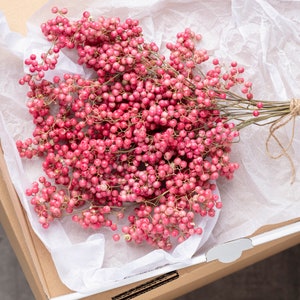 Peut inclure: Un bouquet de baies roses liées avec de la ficelle, présenté sur un fond de papier de soie blanc dans une boîte en carton.