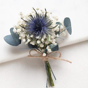 Könnte beinhalten: Ein kleiner Strauß mit einer leuchtend blauen Distel, zartem weißen Schleierkraut und blau-grünen Eukalyptusblättern. Die Stiele sind mit Bindfaden gebunden, was eine rustikale und natürliche Ästhetik erzeugt. Ideal für Hochzeiten oder besondere Anlässe.