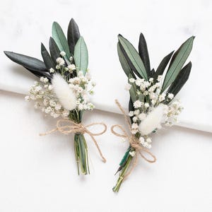 Op de afbeelding: Twee kleine boeketten witte baby's breath en gedroogde bloemen gebonden met touw, met groene bladeren.