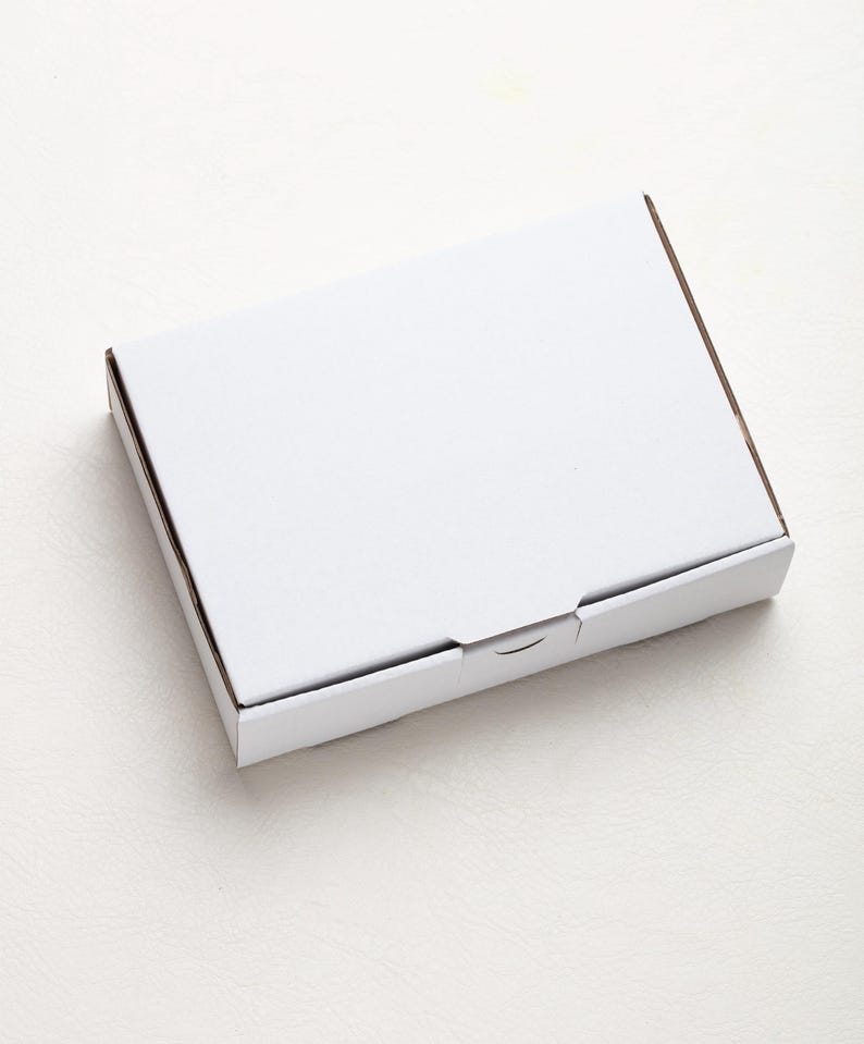 May include: A white, rectangular cardboard box with a closed lid. The box has a simple, clean design, with a smooth, matte finish. The edges of the box are a light brown color.
