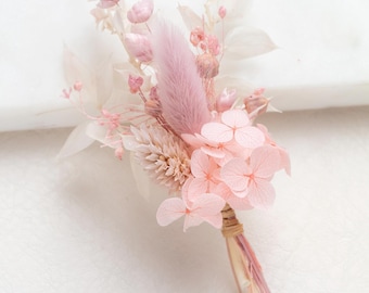 May include: A small bouquet of dried flowers in shades of pink and white. The bouquet includes pink hydrangeas, pink pampas grass, and other dried flowers.