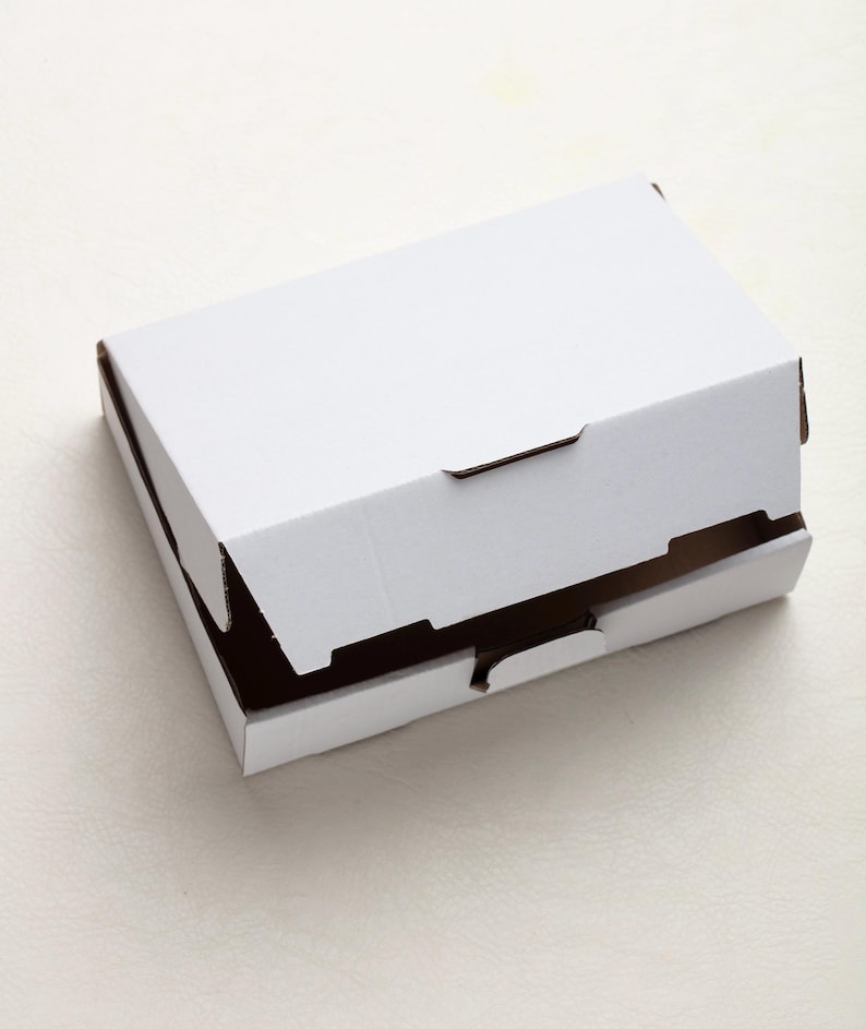 May include: A white cardboard box with a partially open lid. The box is rectangular and has brown edges visible where the lid is open. The box is sitting on a white surface.