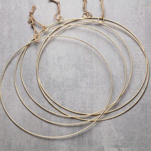 May include: A collection of gold metal wreath rings in varying sizes, suspended by twine. The rings are arranged in a layered pattern, creating a modern and minimalist aesthetic. The background is a neutral gray surface.
