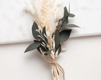 May include: A small, dried flower bouquet featuring cream-colored wheat, fluffy white accents, and dark green eucalyptus leaves. The stems are bound with twine, creating a rustic and natural aesthetic. Perfect for home decor or as a small gift.