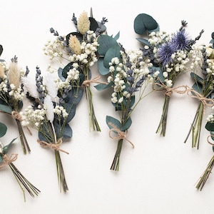 Könnte beinhalten: Mehrere kleine Sträuße aus Trockenblumen, darunter weißes Schleierkraut, Lavendel und Eukalyptusblätter, mit Bindfaden gebunden. Die Sträuße weisen eine Vielzahl von Texturen und Farben auf, vor neutralem Hintergrund.