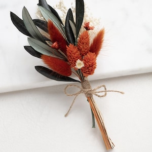 Op de afbeelding: Een klein boeket gedroogde bloemen gebonden met touw. Het boeket bevat oranje en witte bloemen met donkergroene bladeren.