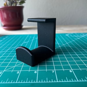 May include: A black 3D printed phone stand with a curved base and a vertical back.