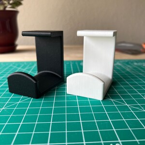 May include: Two 3D printed wall hooks, one black and one white. The hooks are designed to hold items like headphones or cords.