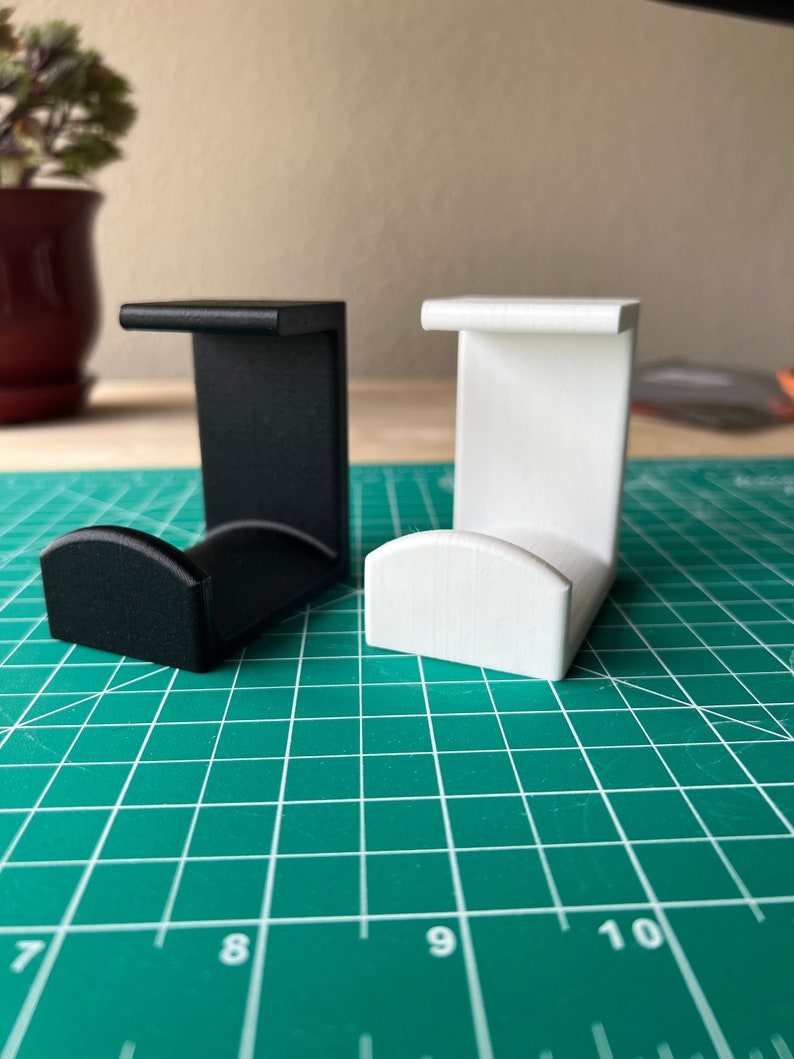 May include: Two 3D printed wall hooks, one black and one white. The hooks are designed to hold items like headphones or cords.