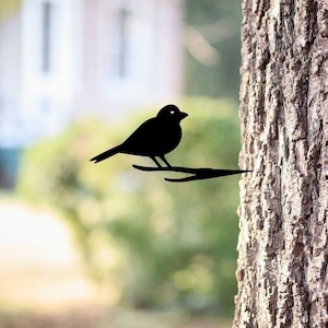 May include: Black metal silhouette of a bird perched on a branch, mounted on a tree trunk.