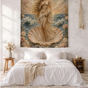 Op de afbeelding: Een rechthoekig wandtapijt met een gestructureerde illustratie in reliëf van een figuur die in een grote schelp staat te midden van oceaangolven. Het kunstwerk toont een gouden zon, een maansikkel en florale accenten in blauwe, crèmekleurige en gouden tinten.