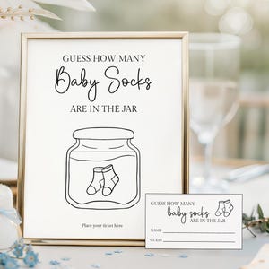 May include: A framed sign with the text "GUESS HOW MANY Baby Socks ARE IN THE JAR" and a drawing of a jar with baby socks. A small card with the same text and space for a name and guess is also present. A champagne flute is in the background.
