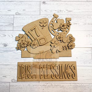 May include: Wooden St. Patrick's Day decoration featuring a leprechaun hat with the number 17, a horseshoe, and shamrocks. The words "IRISH BLESSINGS" are displayed on a separate wooden sign. The design is in a natural wood color.