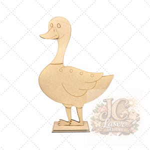 May include: A wooden duck cutout, featuring a long neck, rounded body, and a square base. The duck has a detailed beak and wing design. The image includes the text "JC Laser DESIGNS" in a decorative font.