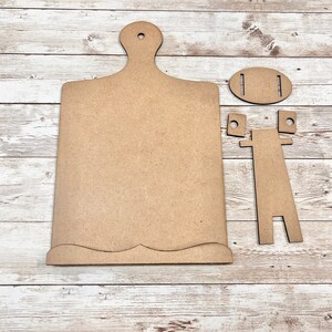 May include: A wooden cutting board with a scalloped edge and a stand. The stand is made of two pieces that fit together to create a vertical stand.
