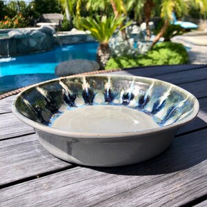 May include: A gray ceramic bowl with a blue and white glaze pattern. The bowl is sitting on a wooden surface.