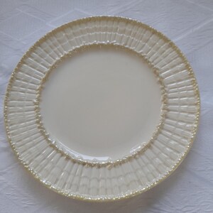 May include: A white ceramic dinner plate with a raised, textured rim in a light beige color.