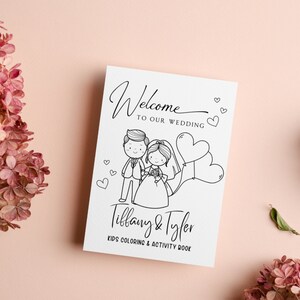 May include: A black and white coloring book with a cartoon bride and groom holding hands. The book says "Welcome to our wedding" and "Tiffany & Tyler Kids Coloring & Activity Book".