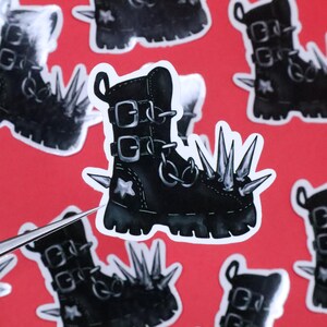 May include: A black leather boot with silver buckles and a chain. The boot has spikes on the toe and heel. The boot is on a white background.