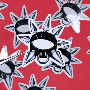 May include: A black and silver spiked collar with a ring on the front. The collar is on a red background with other similar collars.