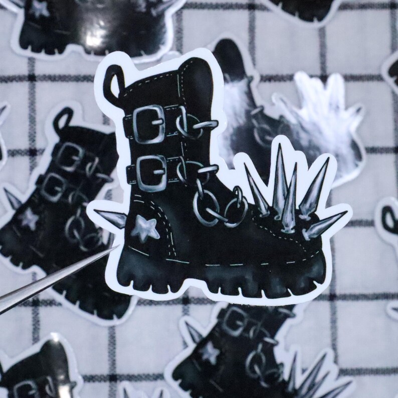 May include: Black and white sticker of a punk rock boot with spikes. The boot has buckles and chains.