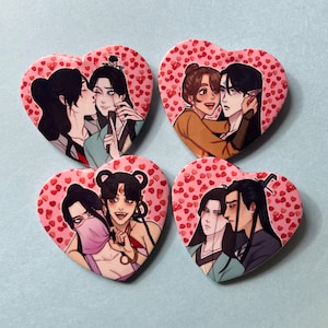 Op de afbeelding: Vier hartvormige pinnen met roze en witte achtergronden waarop stellen te zien zijn. Elke pin heeft een ander stel met verschillende kapsels en kleding. De stellen kijken elkaar allemaal aan en lachen.